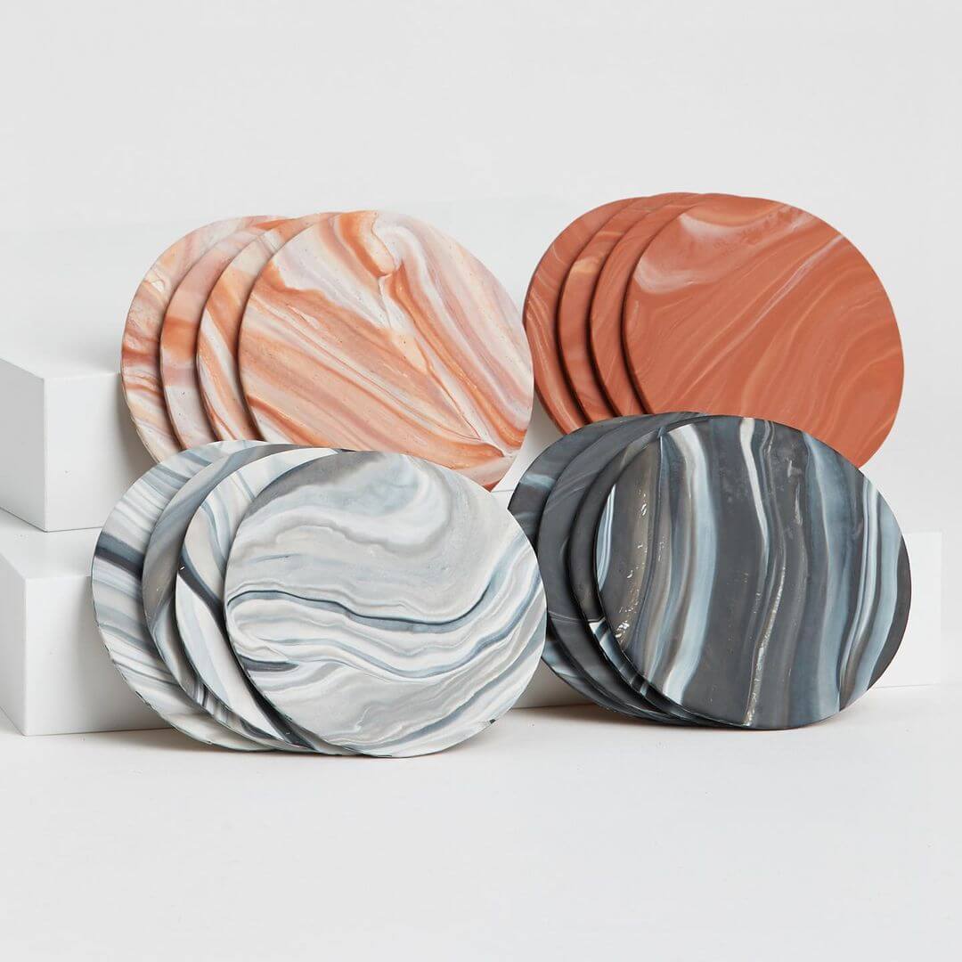 Four marbled drink coasters made from polymer clay in orange, terracotta, grey and black.