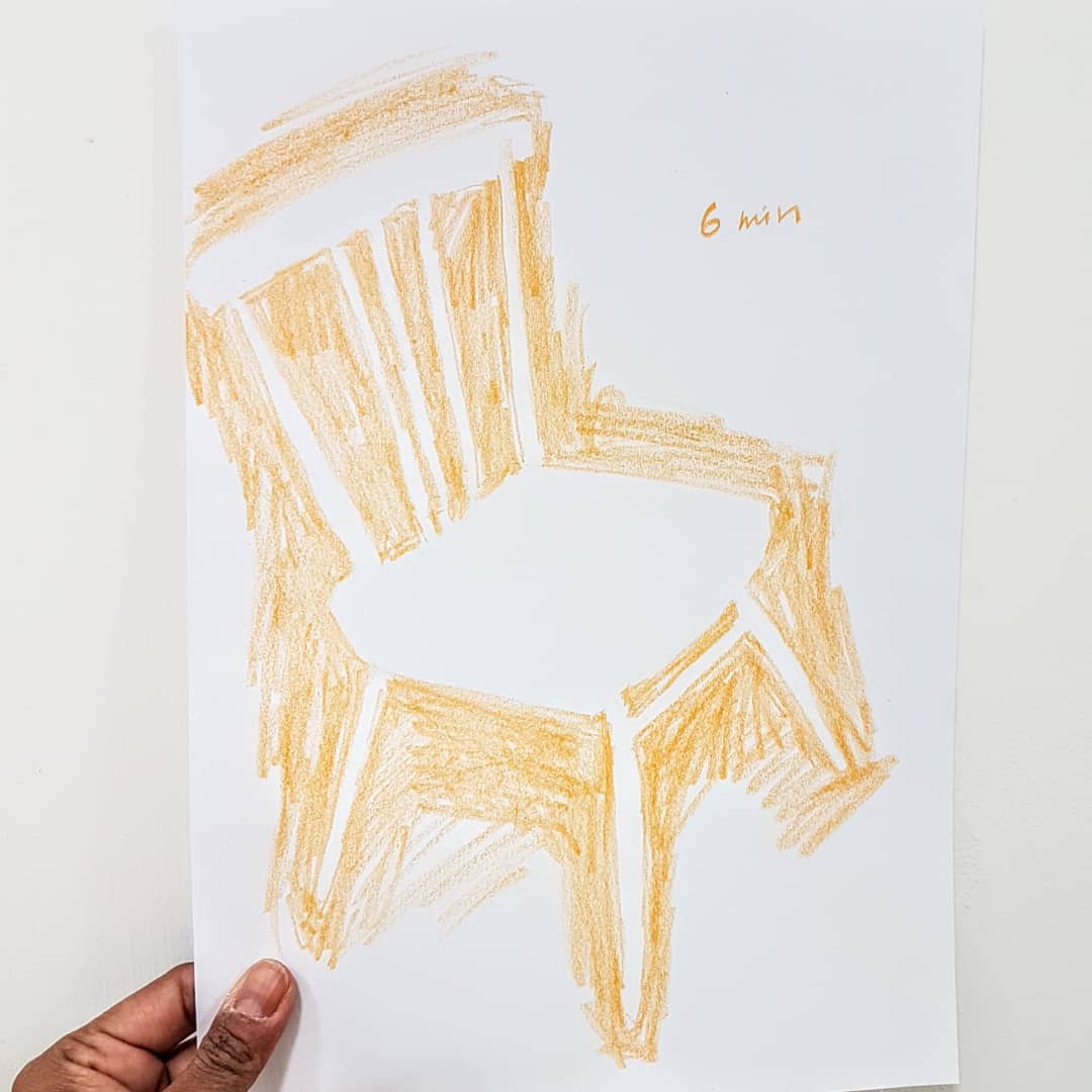 4. Hand holding a drawing of a chair with orange pencil and shading around the chair.