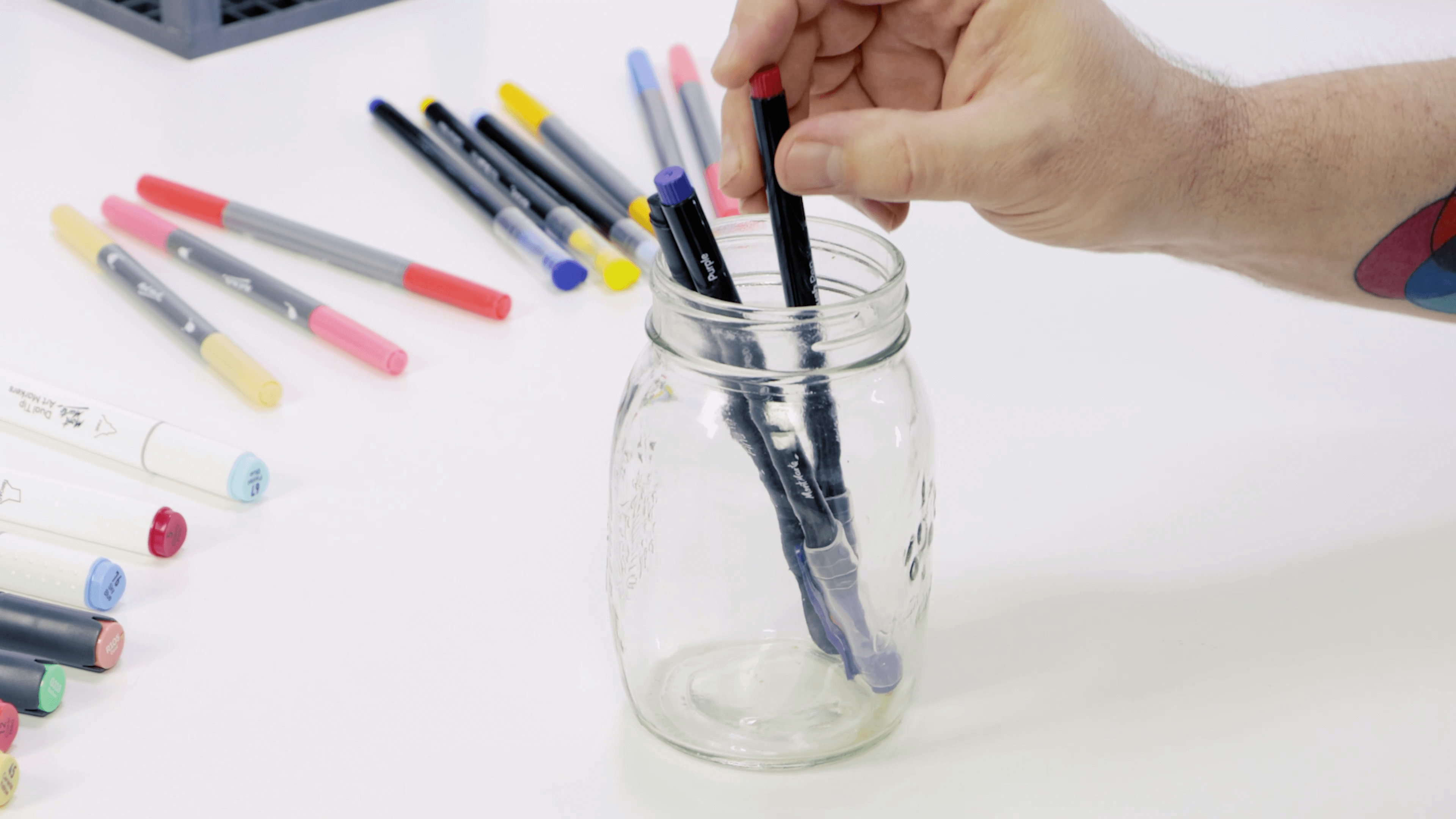 Hand storing art markers in a glass jar.