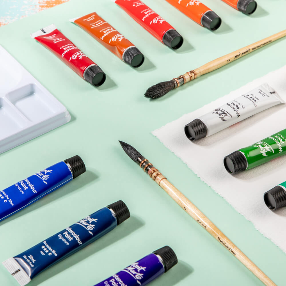 4. Lifestyle picture of watercolour paint tubes with to brushes and mixing wells in frame