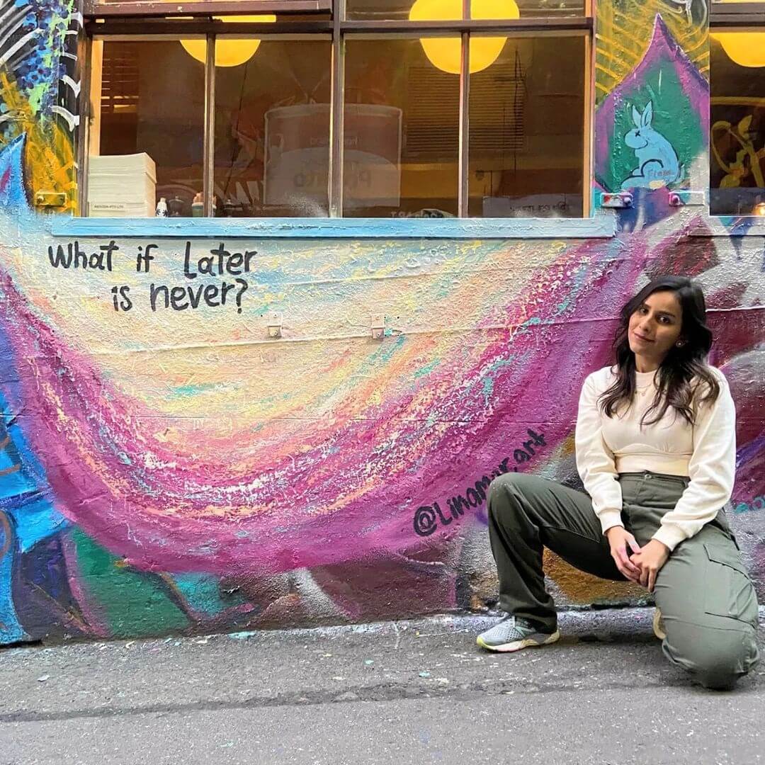Lina in Melbourne's Hozier Lane next to a coloured mural painted on a café window.