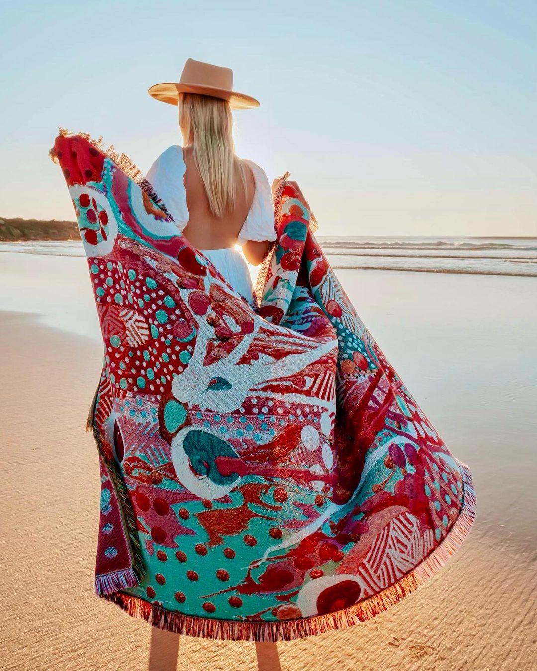 4. Person wearing a hat walking on the beach wih a brightly patterned scarf catching on the wind