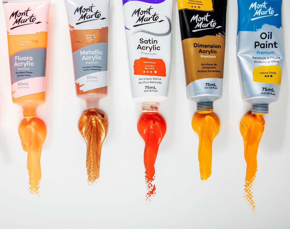 5 different hues of Mont Marte orange paint squeezed out of the tube, onto a white table.