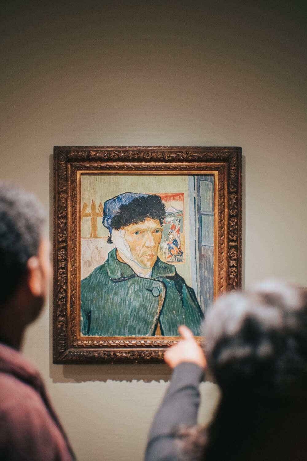 Two people pointing to Self-Portrait with Bandaged Ear by Vincent van Gogh in an art gallery.