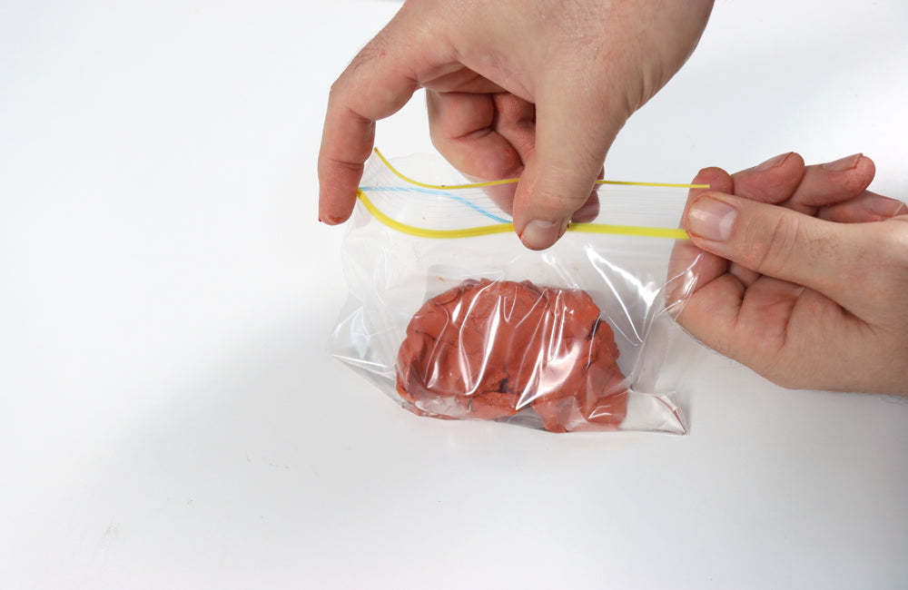 Hand closing zip lock bag with air dry clay to keep it fresh.