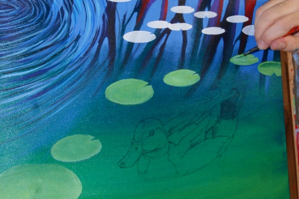 Hand painting lily pads on a lake with a duck drawing below the lily pads.