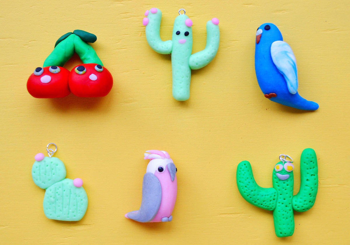 Various cute polymer clay pendants of a cherry, cactus and birds.