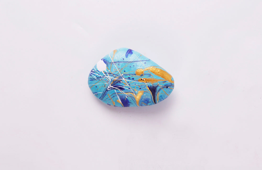 Small rock painted in blues, gold and white pouring paint