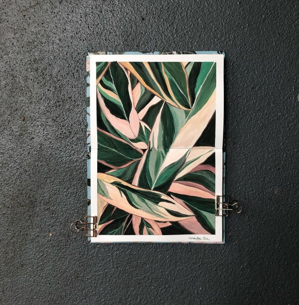 A gouache artwork of a leaf laying on a black table.