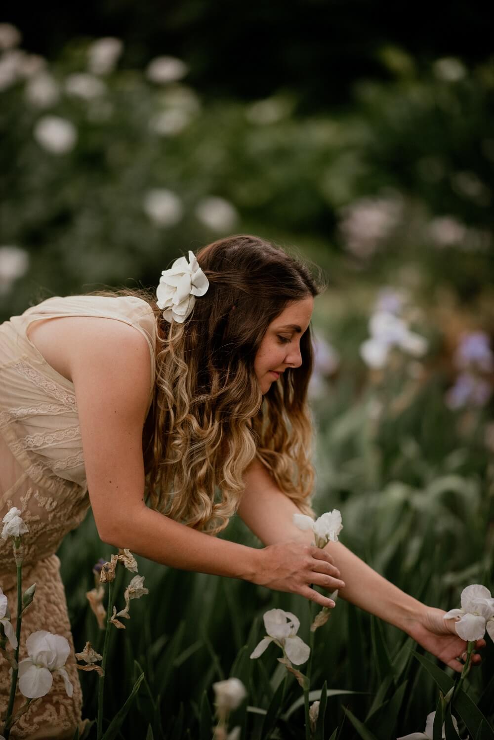 Chelsea from Chelsart picking white flowers in a field with flowers in hair.