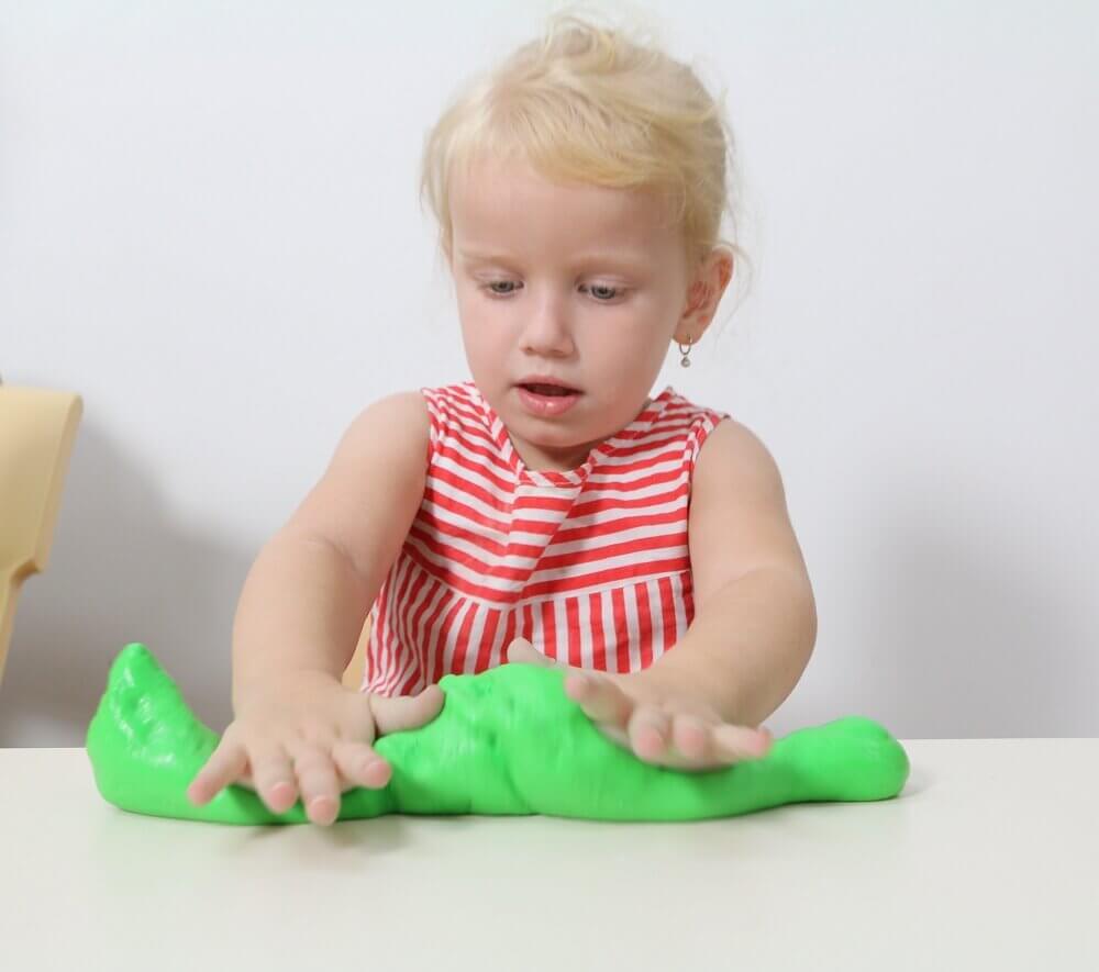 Girl rolls out the finished glitter slime on a white bench.