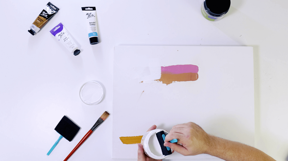 Hand holding a foam sponge brush, applying gesso to an acrylic painted surface.