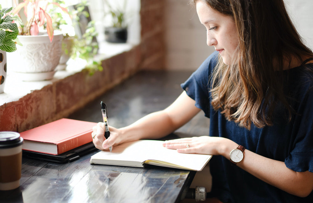 Female drawing in a notebook next to a balcony.