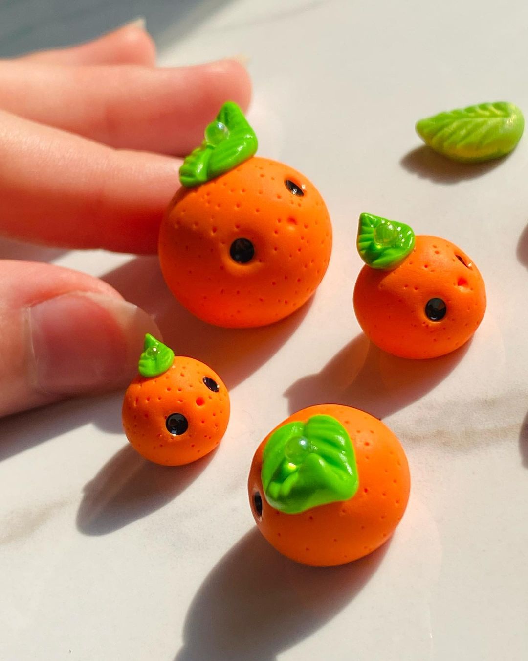 4 small orange sculptures with faces and leaves on their heads
