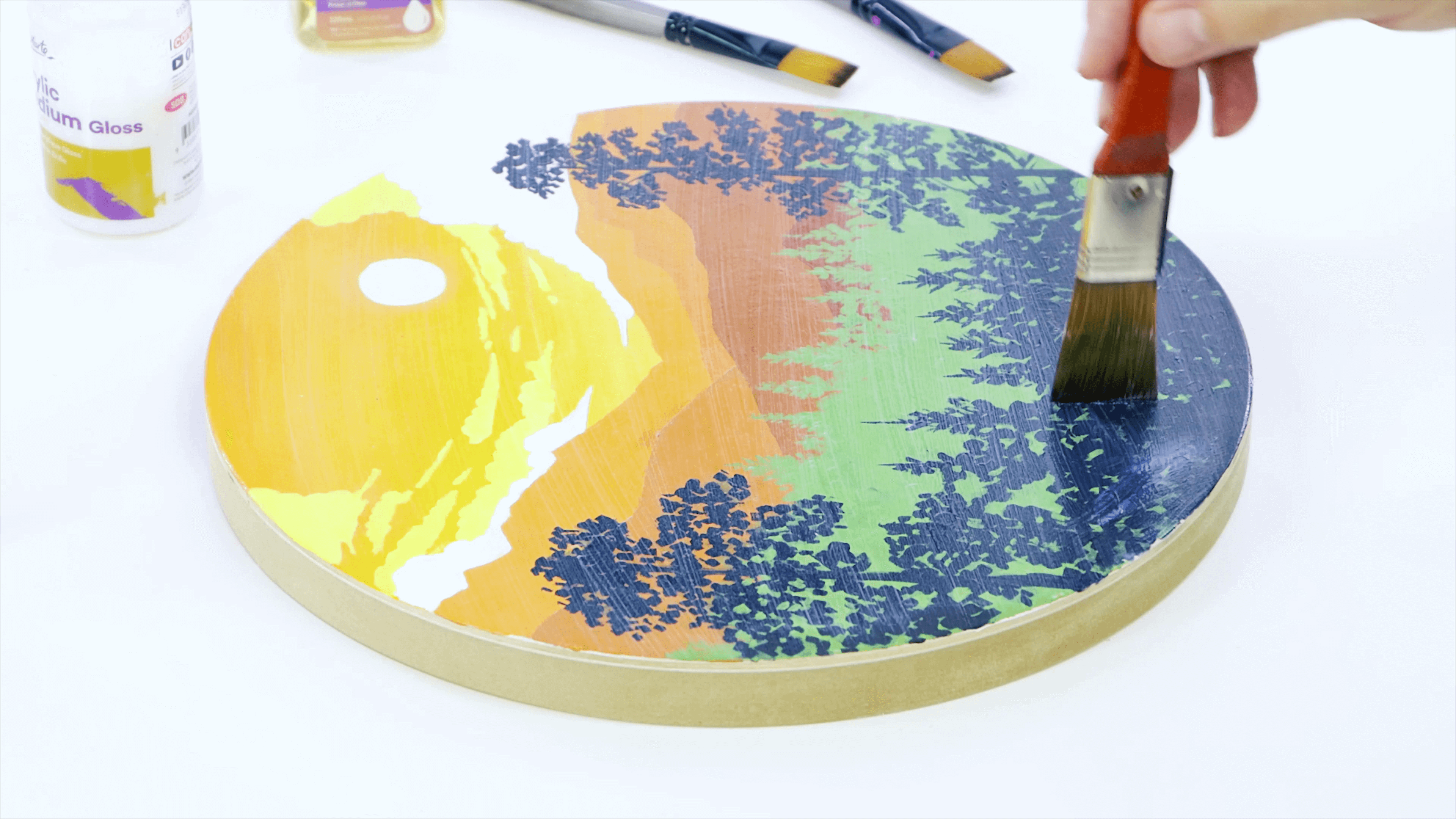 A circular artwork of a forest with a red paintbrush applying varnish over the top.