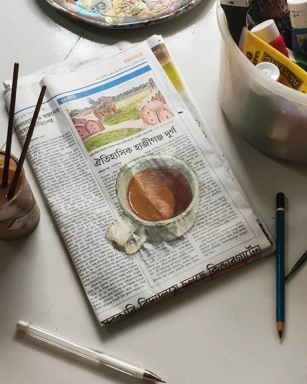 A newspaper with a coffee cup painted on top, next to a pencil, paints and brushes.