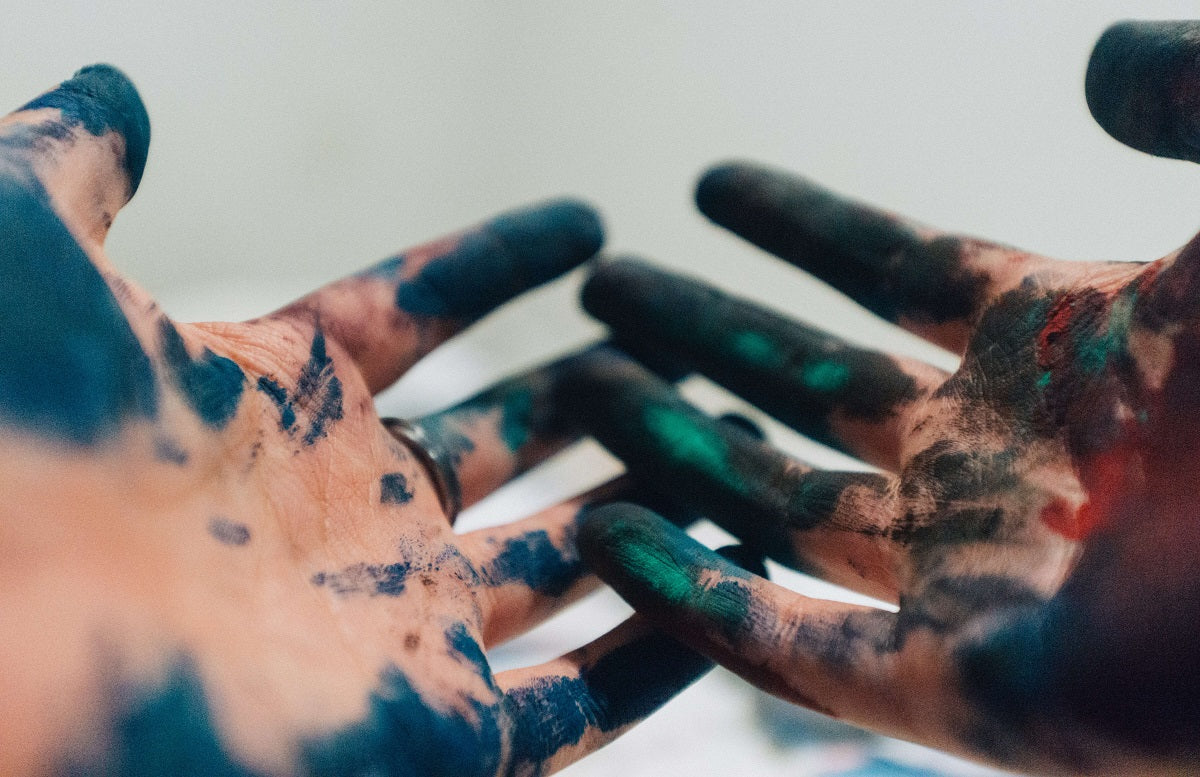 A person's hands with dried green and navy paint all over their hands.