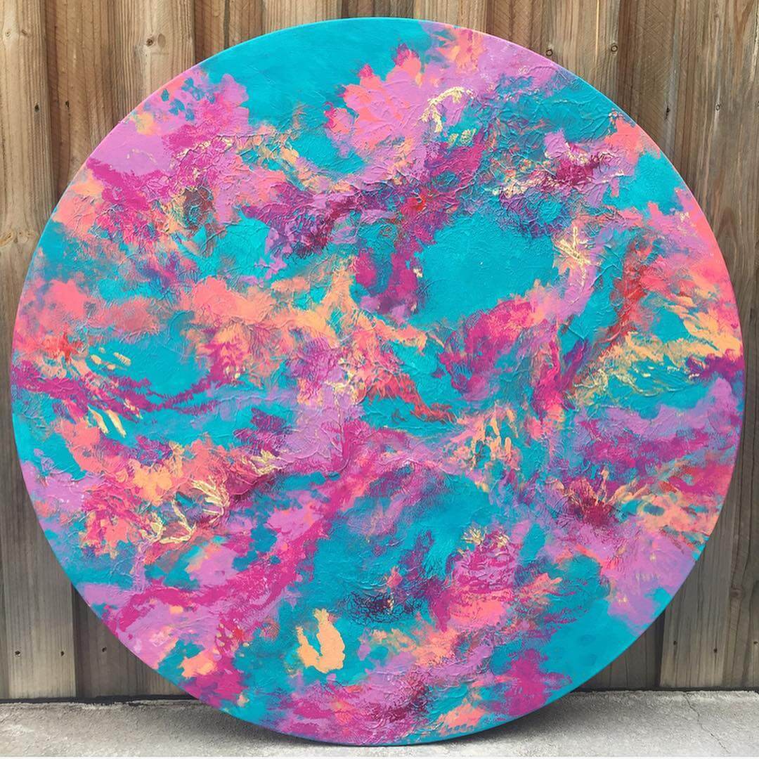 A round canvas with turquoise, pink, coral and peach paint painted in an abstract style.
