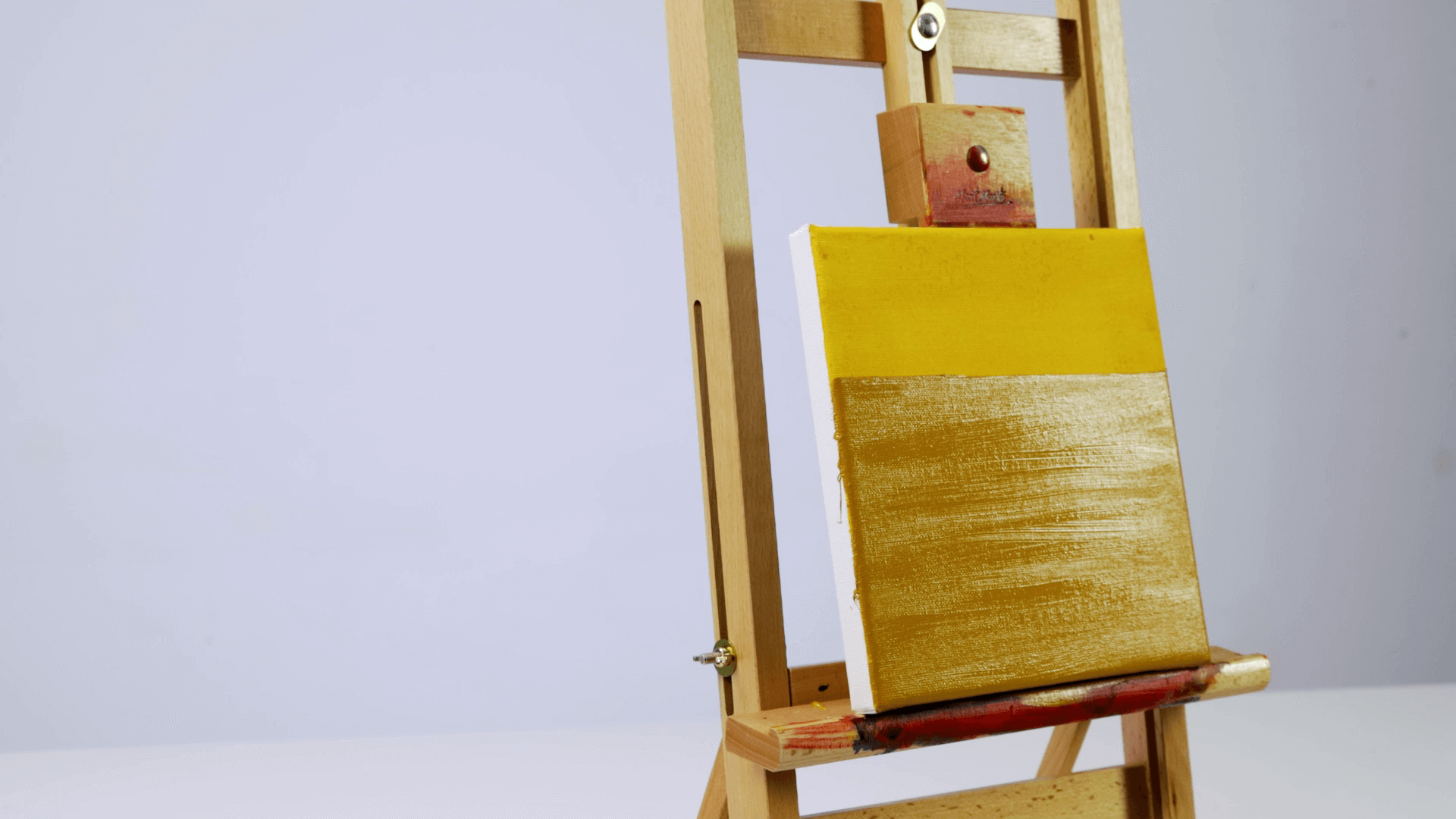 A yellow canvas on a wooden easel that is painted with oil paints showing the fat over lean technique with layers of oil paint.