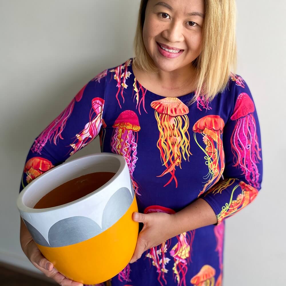 Ann in a bright jellyfish dress holding a yellow painted pot plant.