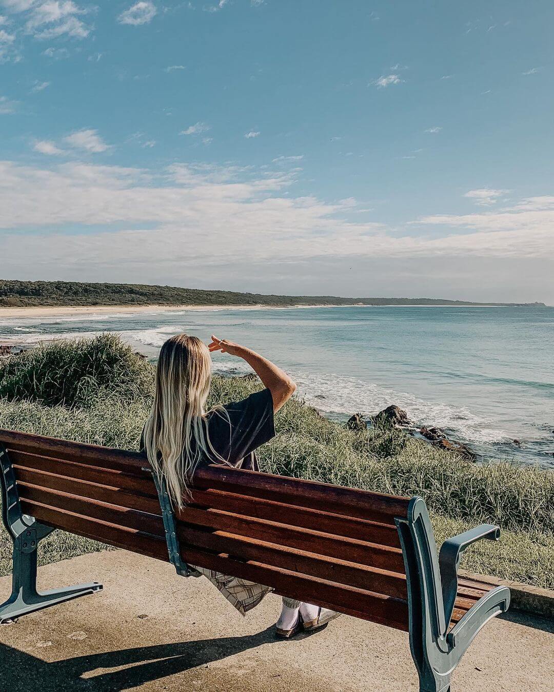 Artist Jess sitting on a park bench at the beach.