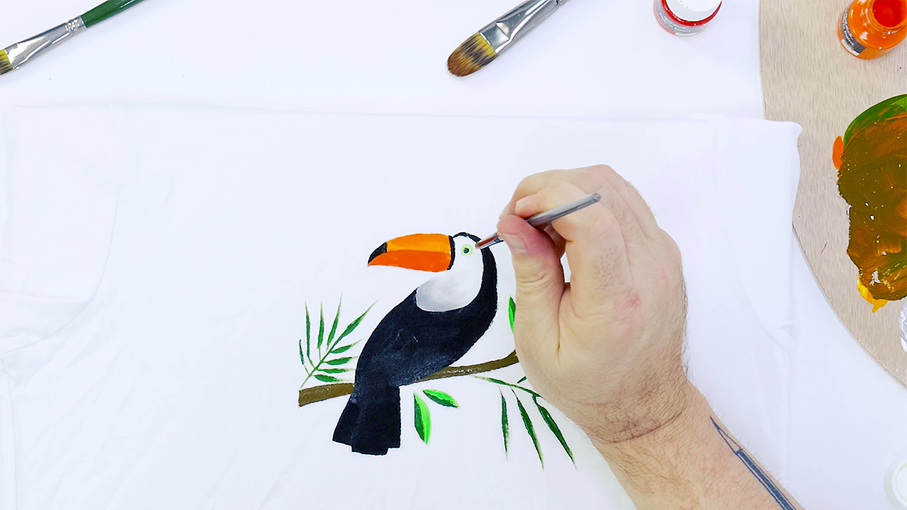 Hand painting toucan on a white t-shirt using fabric paints and a taklon brush.