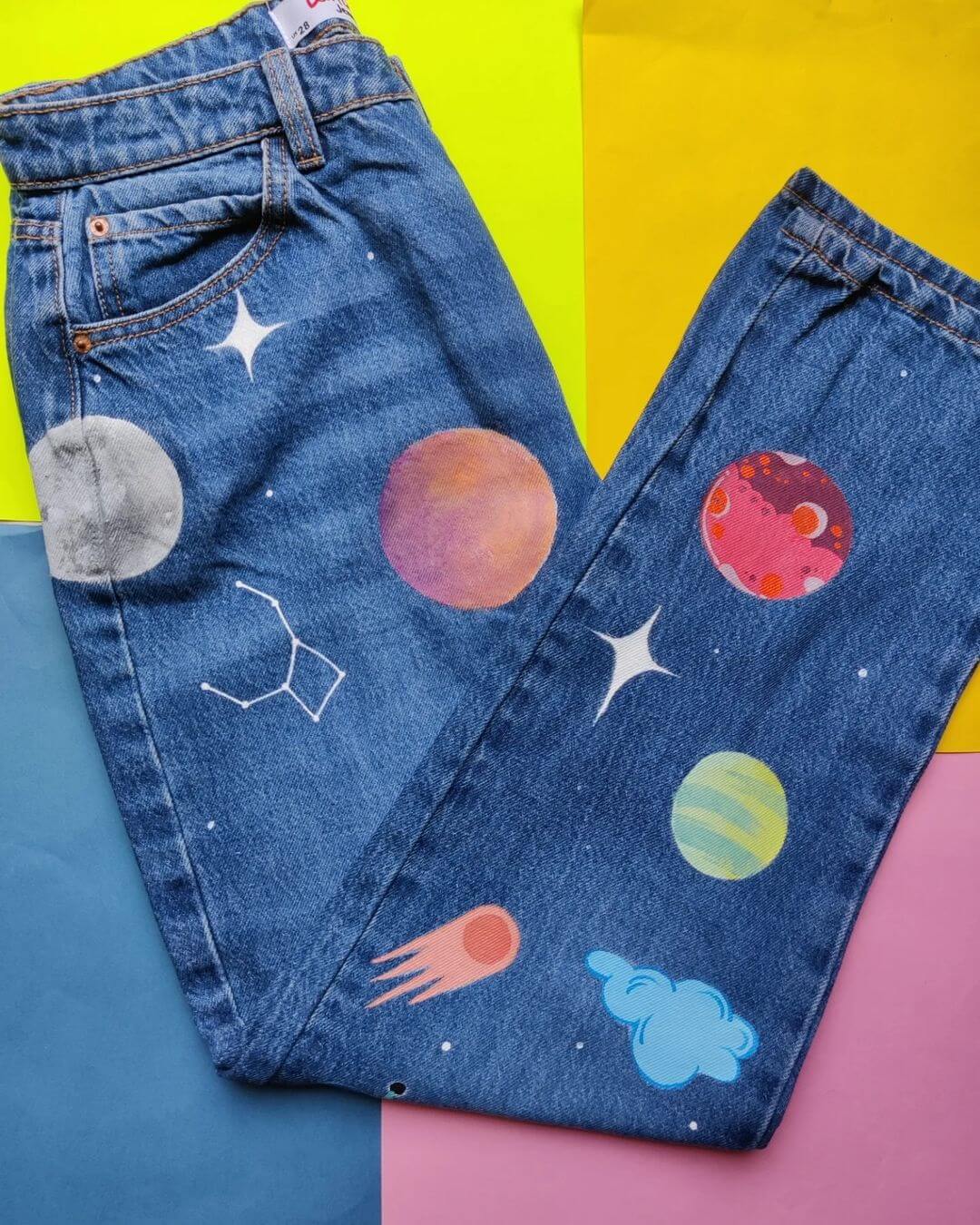 Pair of blue jeans with planets and stars painted on top.