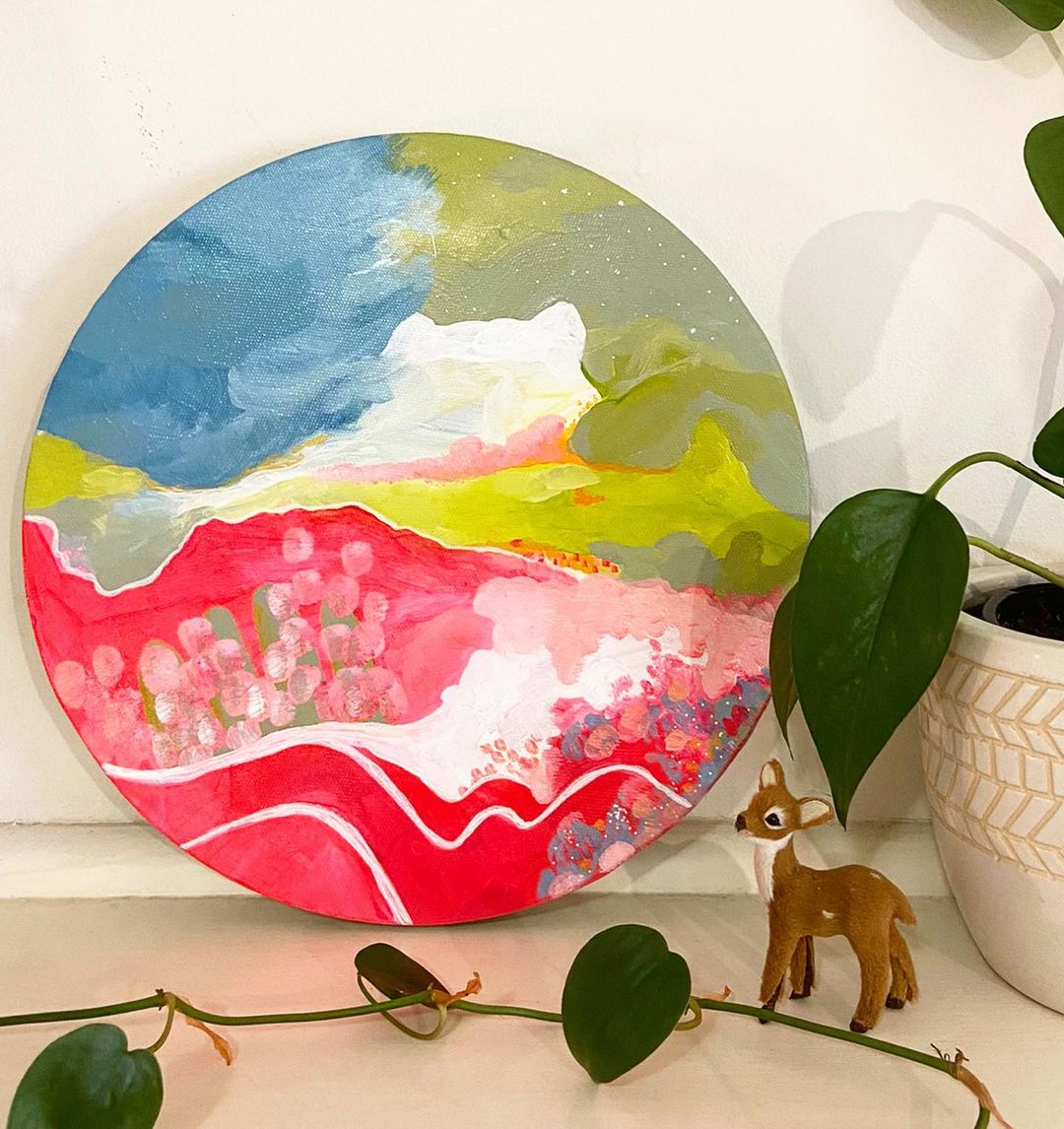 Tessa's artwork 'abstract porthole #6' on a circular canvas next to a small plastic deer and plant leaves near by.