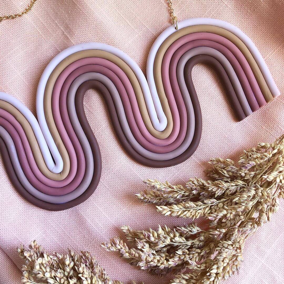 Various shades of mauve clay made into an arched wall hanging next to dried flowers.