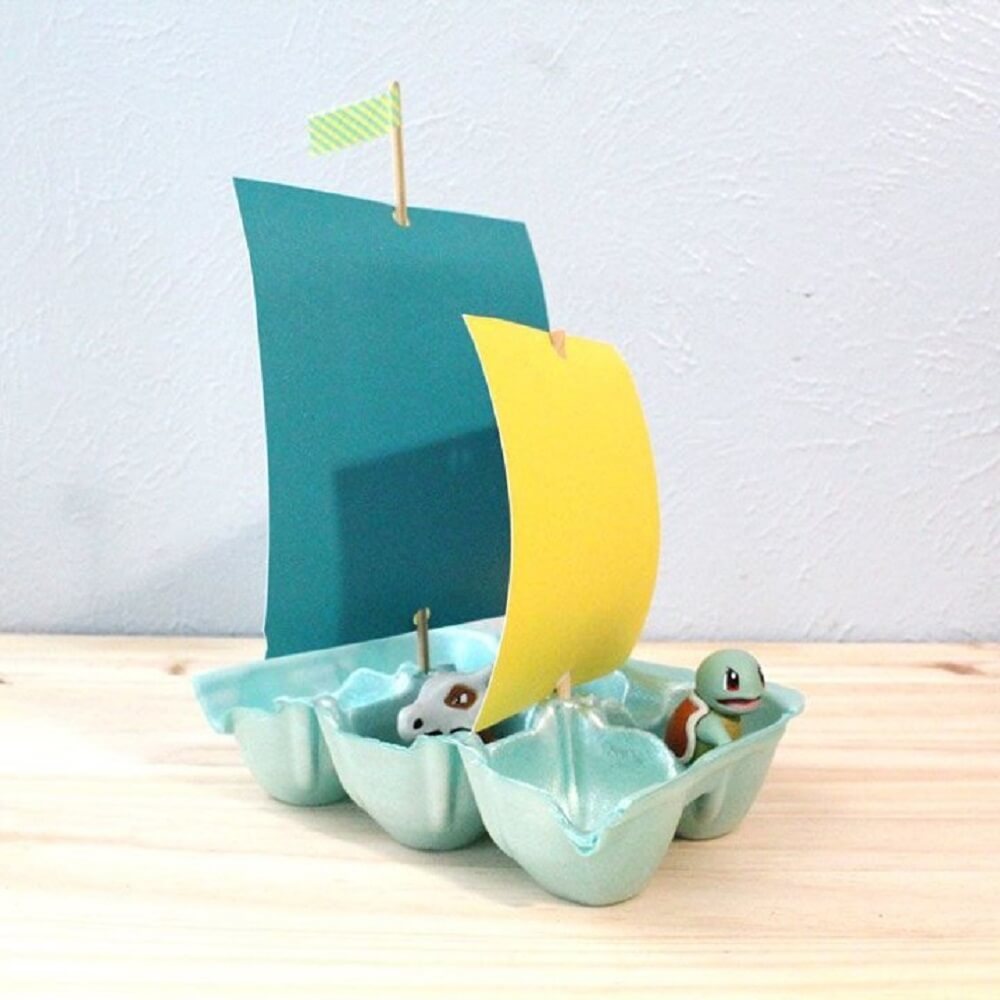 An egg carton made into a boat with yellow and blue flag.