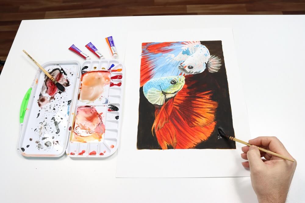 Hand adding the final touches to a Betta fish watercolour painting using watercolour tubes.