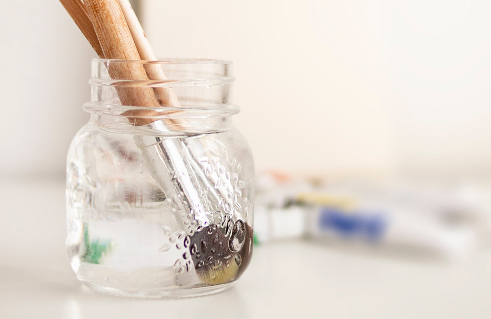 Two paint brushes in clear water jar.