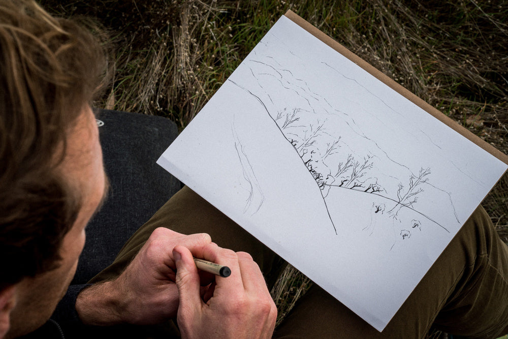 A man drawing a cityscape in a notebook.