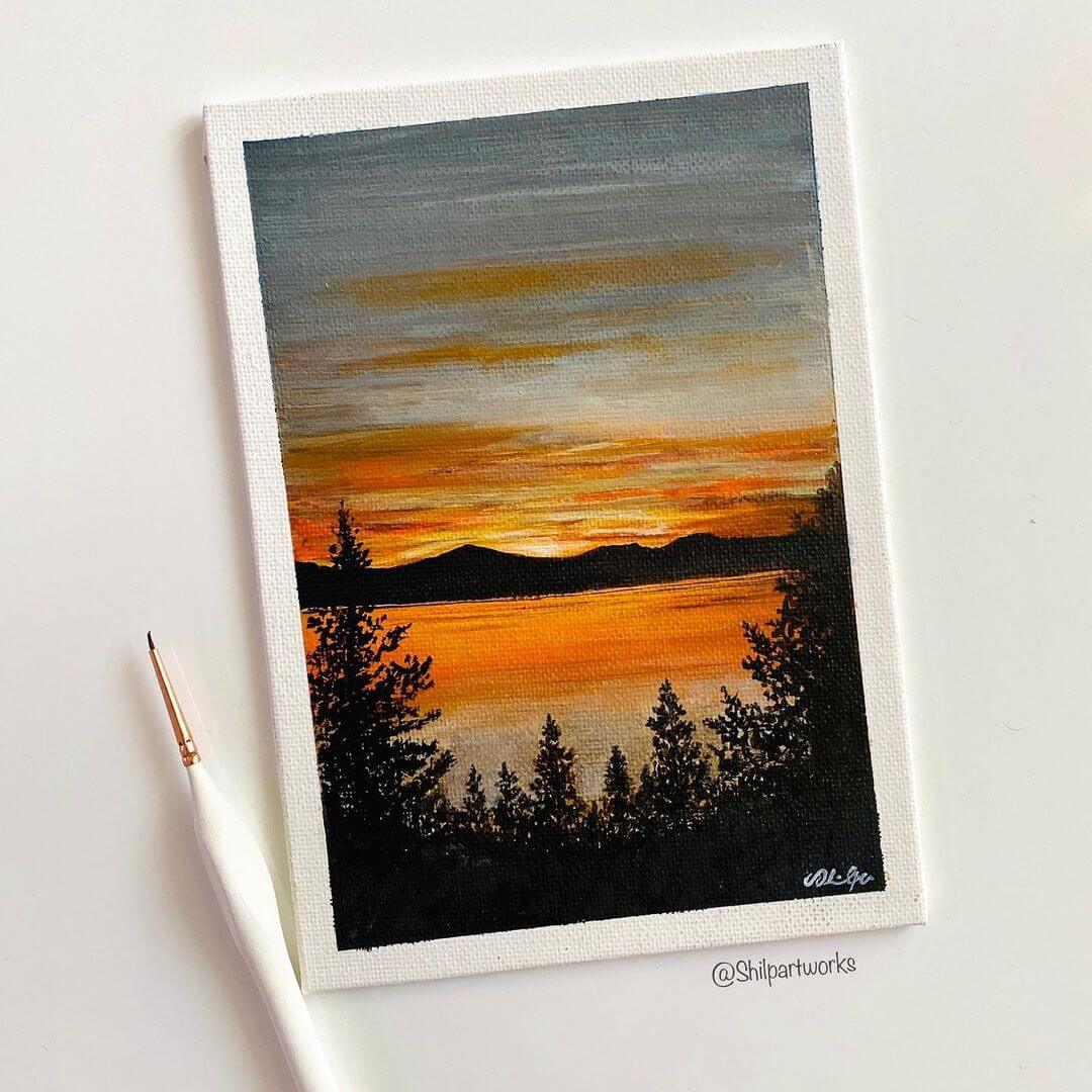 6. A painting of a landscape at sunset with a white paint brush next to it.