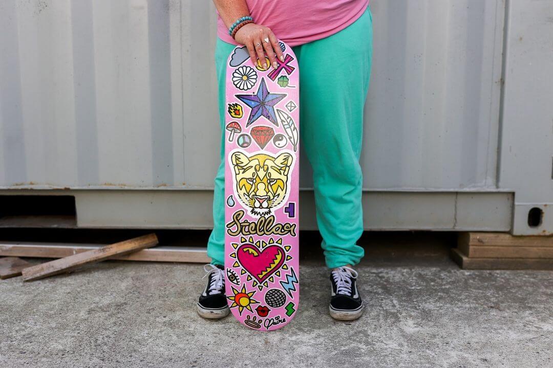 6. Claire holding a pink skateboard with 90's style pained decals painted on it.