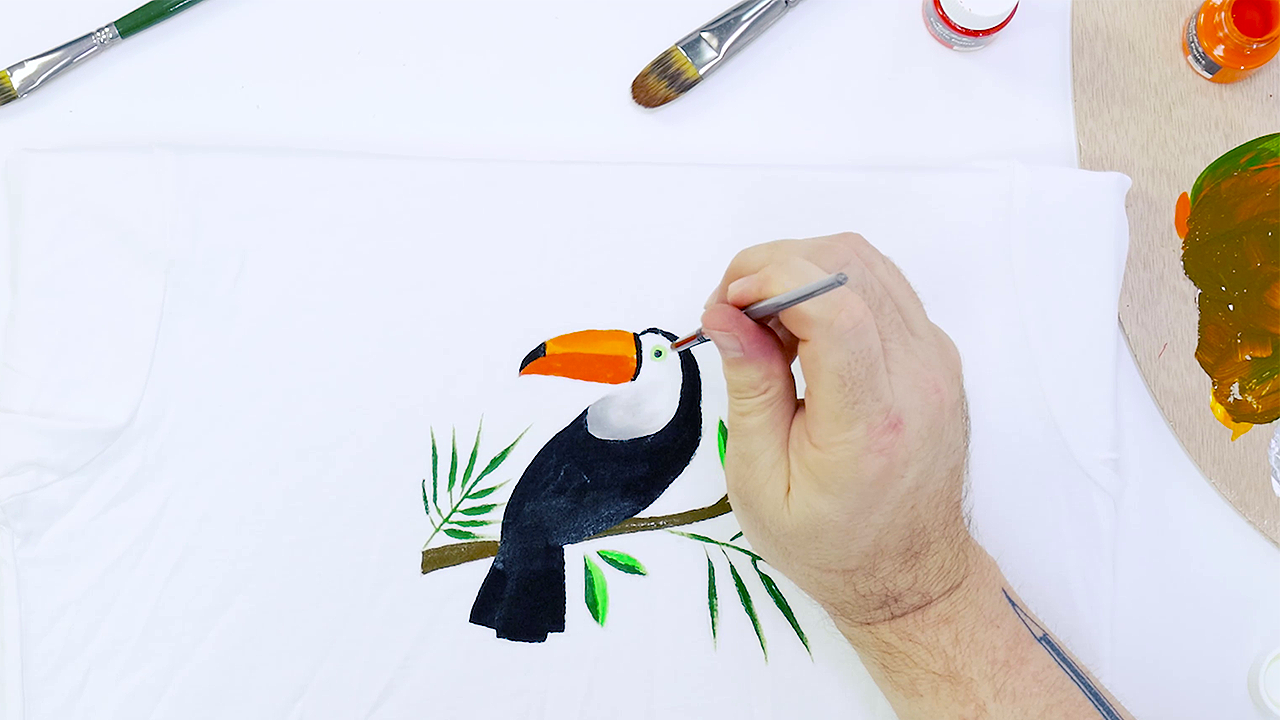 Hand free painting a toucan on a white tshirt using fabric paints.