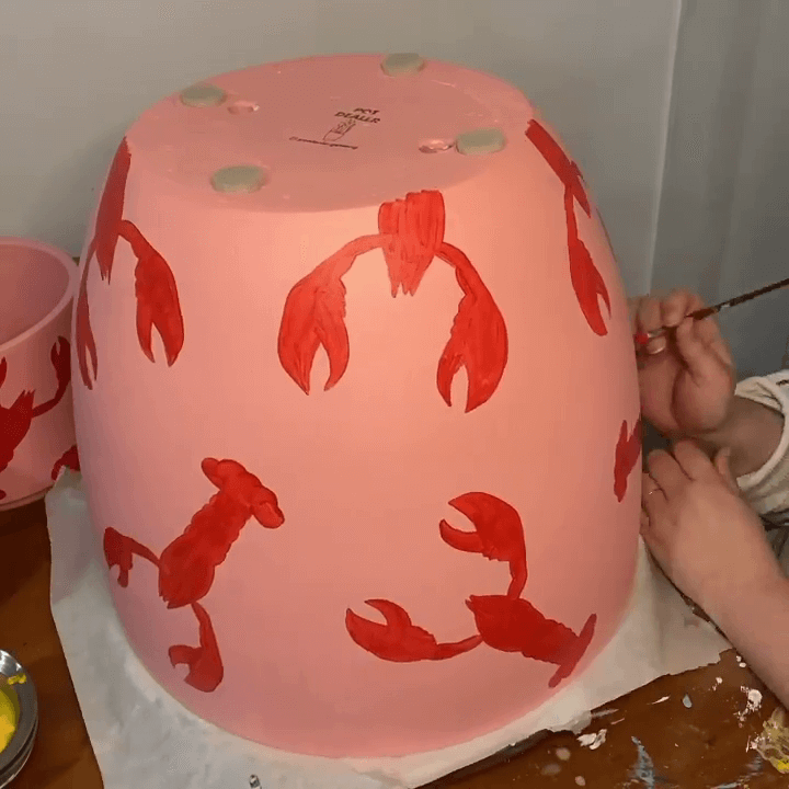 Hand painting red lobsters on a pink terracotta pot.