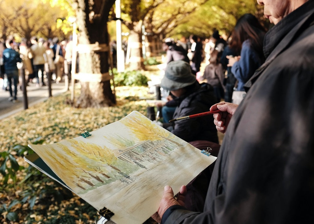 Man painting watercolours en plein air in a busy park.