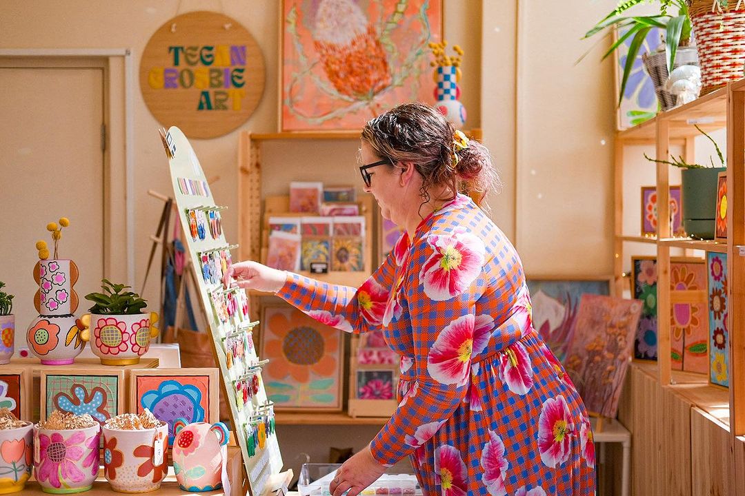 6. Tegan displaying brightly designed earrings in The Workshoppery surrounded by artwork