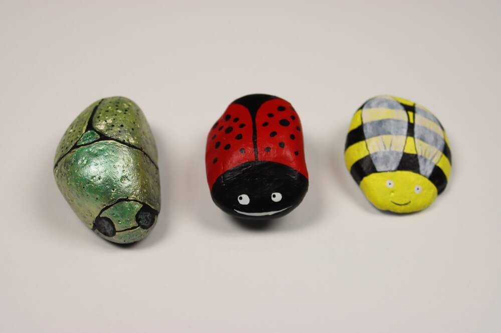 Three rocks painted as insects. A Christmas beetle, ladybug and bee.