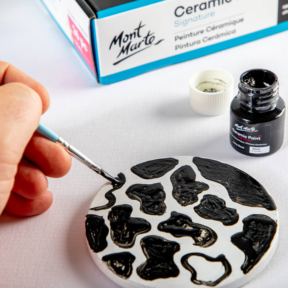6. Using black ceramic paint to create a cow print coaster design