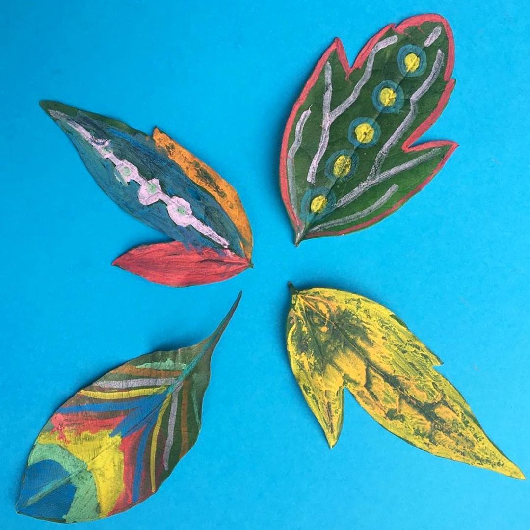 6. @theamazingartcart Green leaves painted with rainbow colours against a blue background