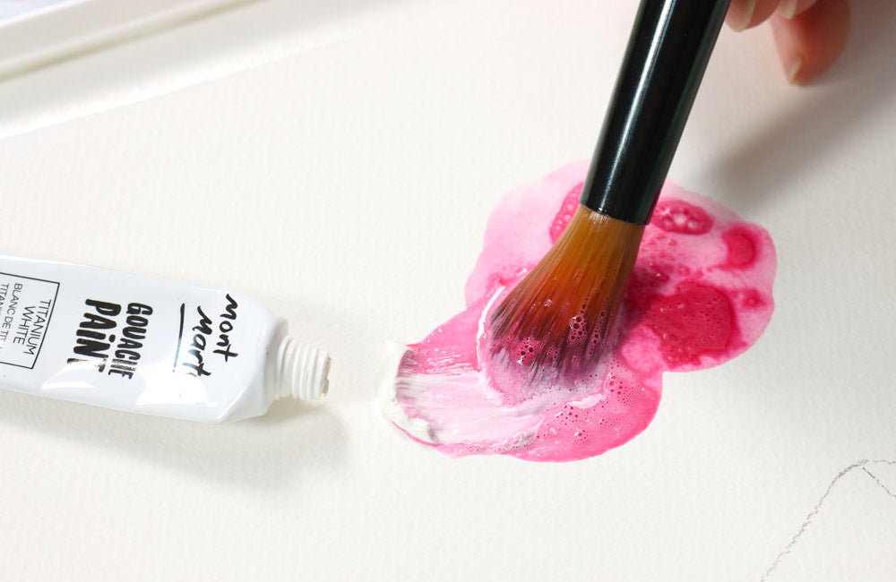 Paint brush mixing white gouache into red water colour paint creating a pastel pink colour.