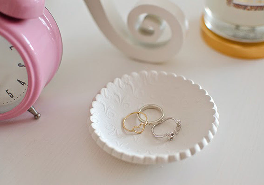 Trinket dish with gold rings inside next to a pink alarm clock.