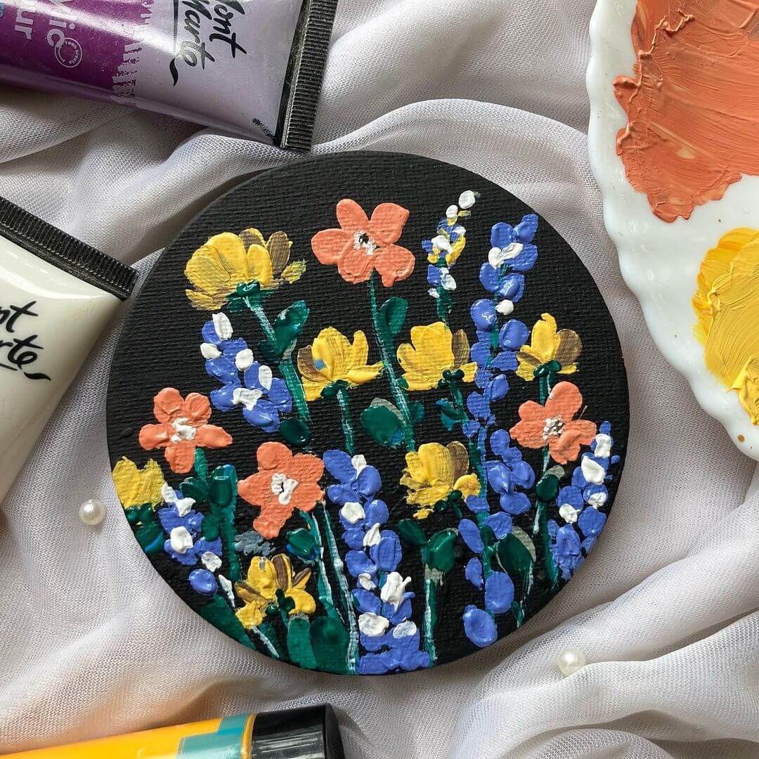 7. A black round palette with abstract painted flowers beside Mont Marte acrylic paints