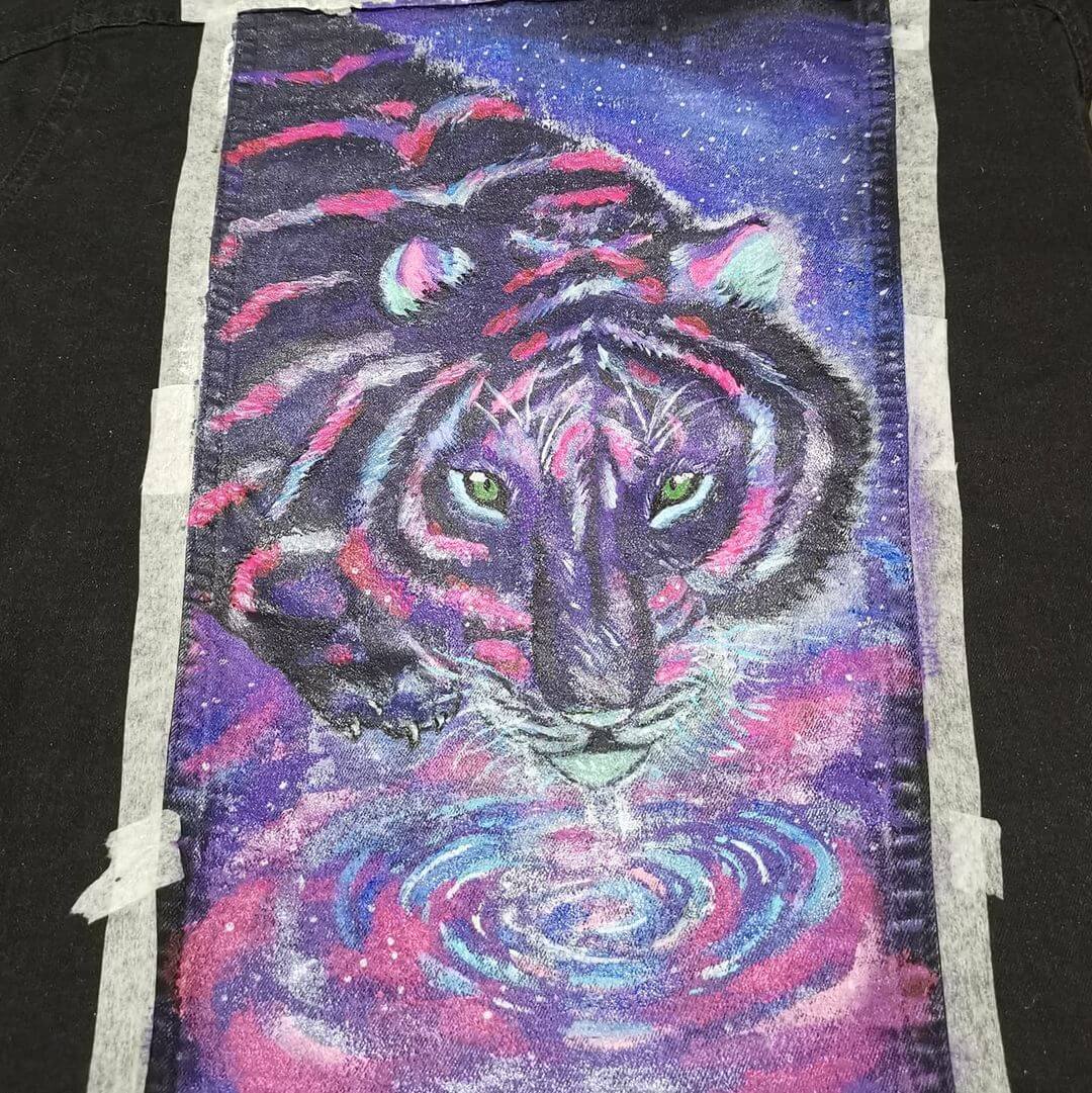 A bright purple and pink tiger that has been painted on the back panel of a black denim jacket.