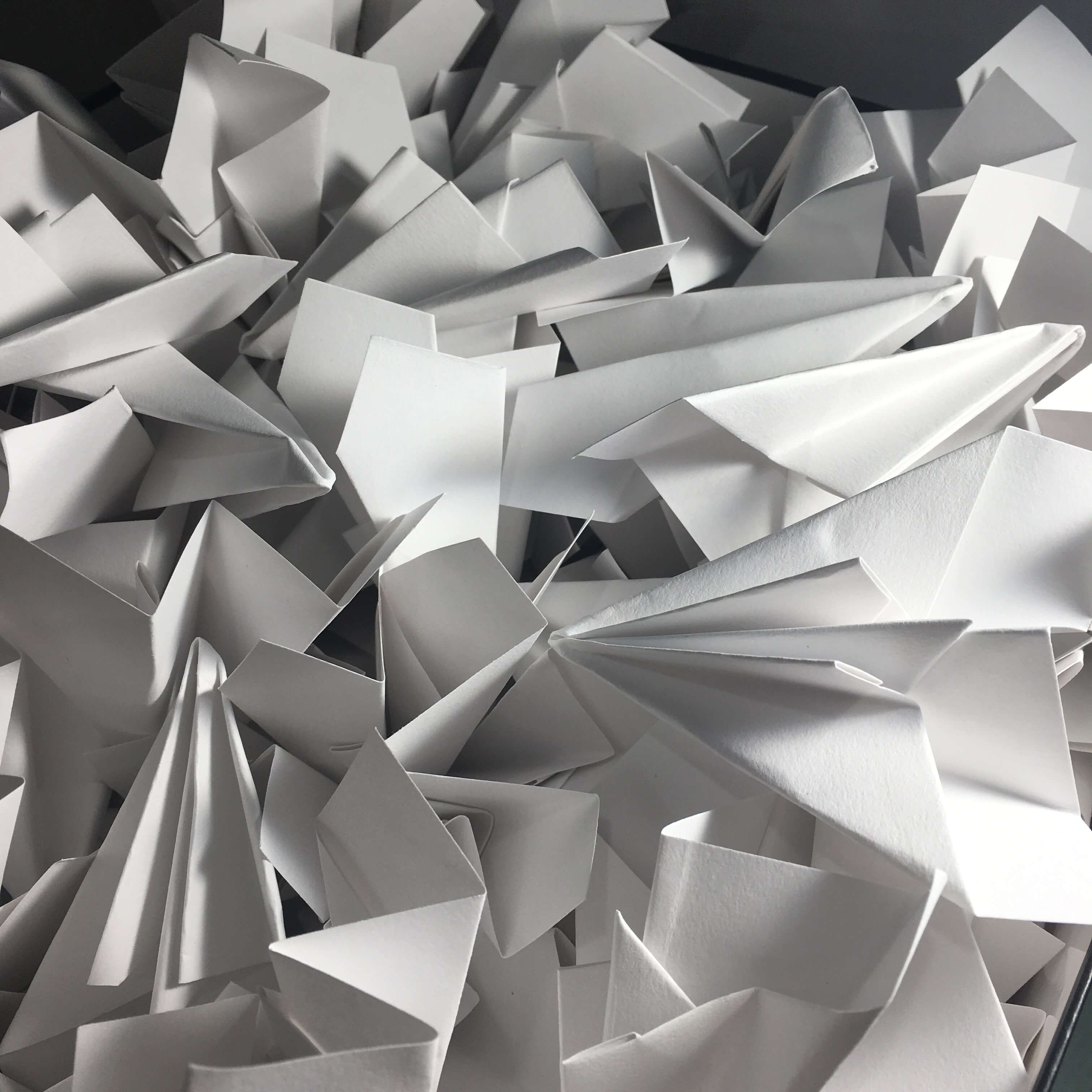 A heap of paper planes made from white paper bunched together.