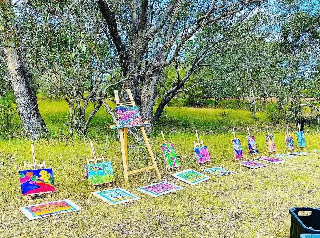 7. An art easel outside with various painted canvases laying on the grass beside it.