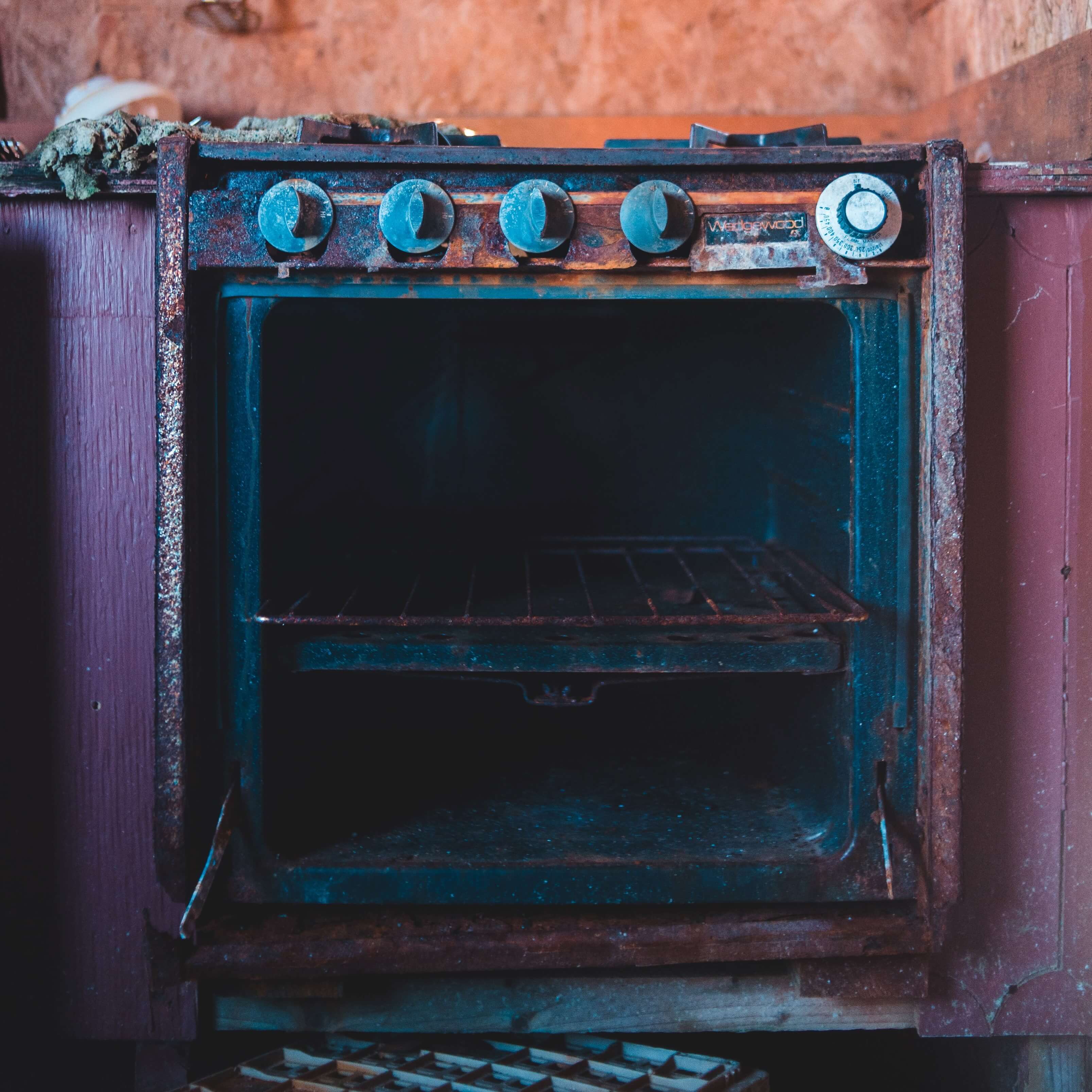 An old purple oven with the door open in an orange brick kitchen.