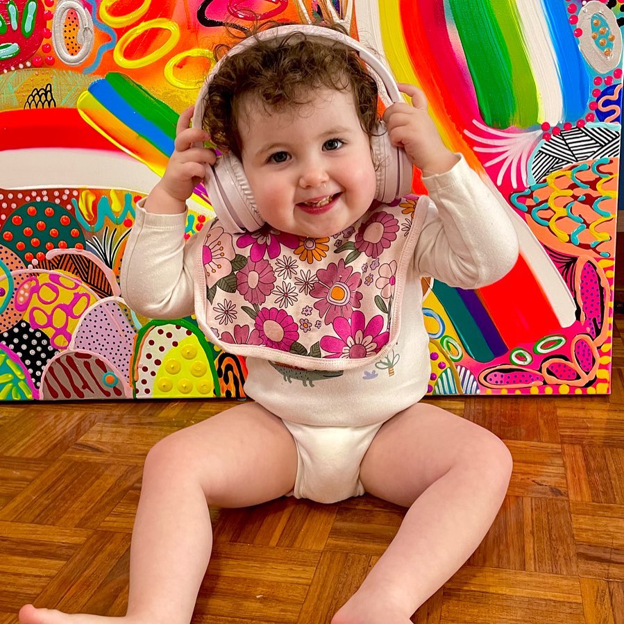 7. Emma's young daughter Odette with headphones on in front of a rainbow coloured painting